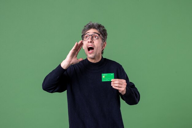 Ritratto di un uomo geniale che tiene in mano una carta di credito verde sulla parete verde