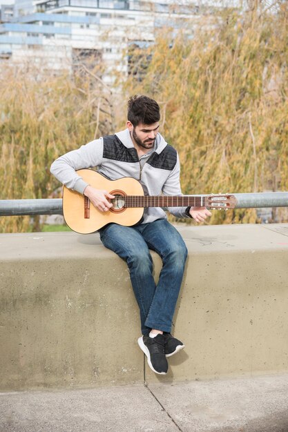 Ritratto di un uomo seduto sul muro di sostegno a suonare la chitarra