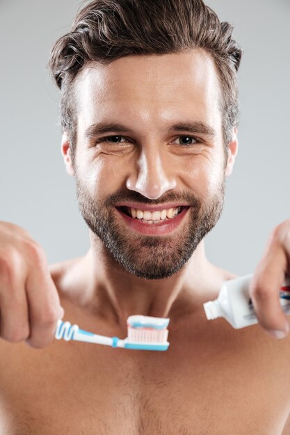 Ritratto di un uomo sorridente che mette dentifricio in pasta su uno spazzolino da denti