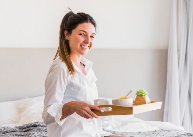 Ritratto di un vassoio sorridente della prima colazione della tenuta della giovane donna