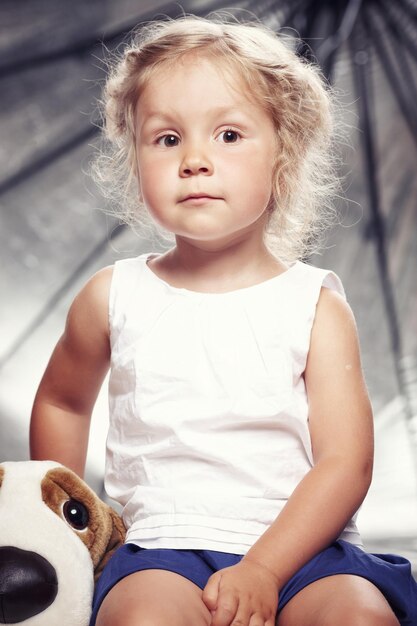 Ritratto di una bambina carina in abito casual seduto con un peluche in uno studio.