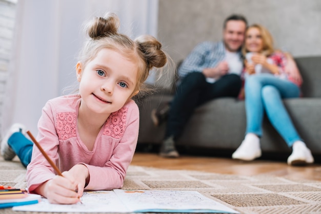 Ritratto di una bambina che attinge libro con i suoi genitori nel fondo vago