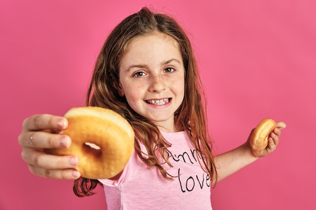 Ritratto di una bambina che offre una ciambella su uno sfondo rosa