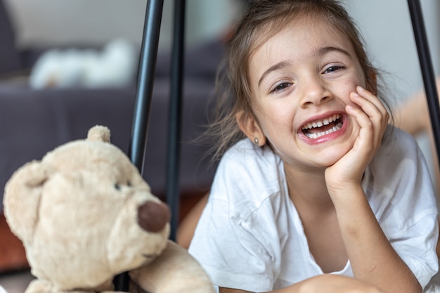 Ritratto di una bambina che ride vicino a un orsacchiotto a casa.