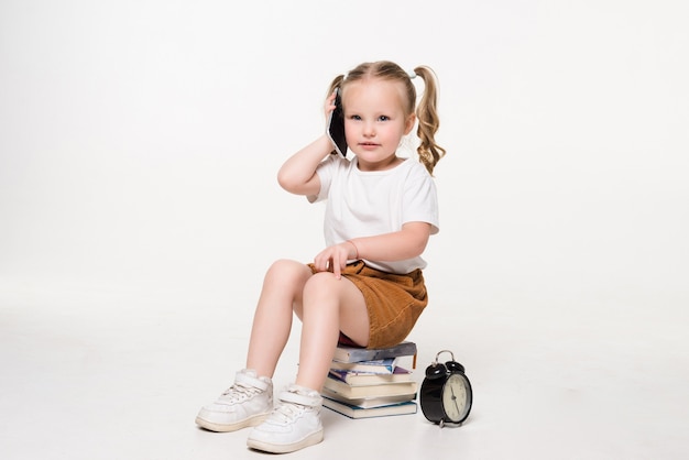 Ritratto di una bambina parla al telefono seduto su una pila di libri.