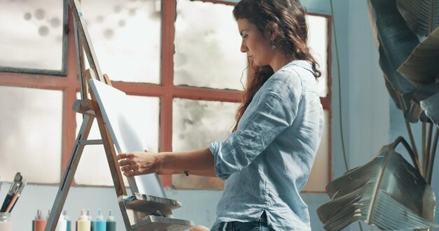 Ritratto di una bella artista femminile dai capelli lunghi al lavoro sulla sua tela in uno studio