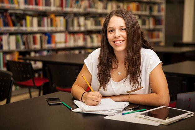 Ritratto di una bella bruna con i capelli ricci che fa dei compiti a scuola e sorride