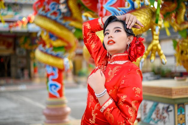 Ritratto di una bella donna asiatica che indossa un cheongsam sorridente e posa con un gesto di congratulazioni al santuario il capodanno cinese
