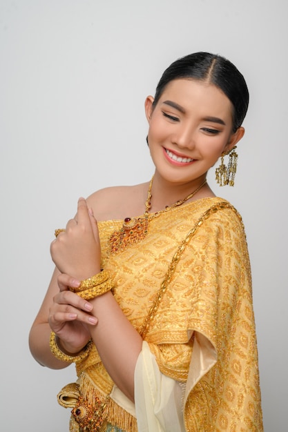 Ritratto di una bella donna asiatica in costume tradizionale tailandese, sorride e posa con grazia sul muro bianco