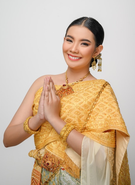 Ritratto di una bella donna asiatica in costume tradizionale tailandese, sorride e posa con grazia sul muro bianco