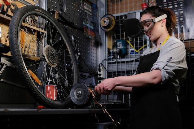 Ritratto di una bella donna bruna che indossa abiti da lavoro, grembiule e occhiali, lavorando su una macchina per affilare in un'officina.