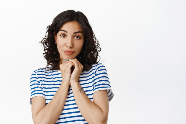 Ritratto di una bella donna castana che guarda, sembra adorabile e romantica, ammira la bella scena, in piedi in t-shirt su bianco.