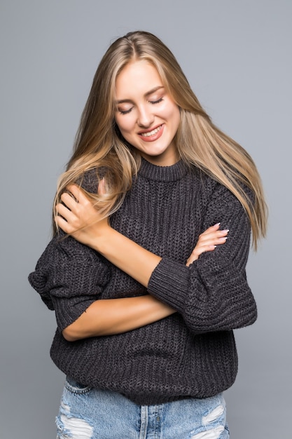 Ritratto di una bella donna che indossa un maglione lavorato a maglia caldo sul suo corpo su uno sfondo grigio isolato