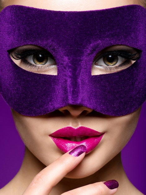 Ritratto di una bella donna con unghie viola e maschera teatrale sul viso.