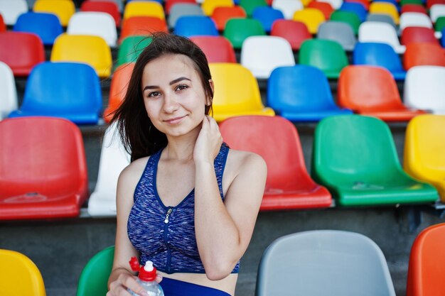 Ritratto di una bella donna in abiti sportivi seduti e acqua potabile nello stadio