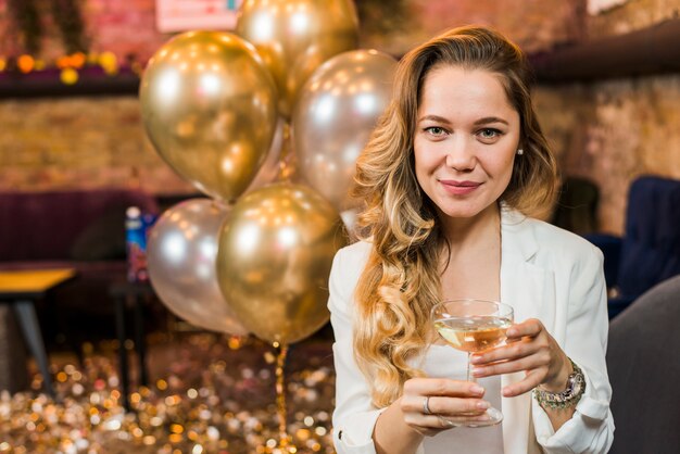 Ritratto di una bella donna sorridente con un bicchiere di whisky in festa