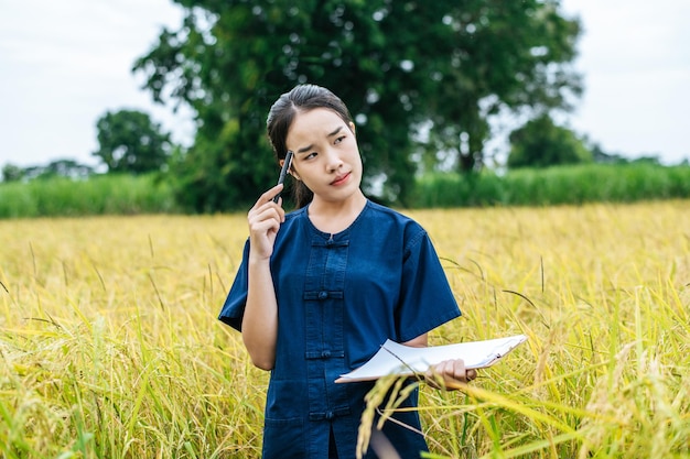 Ritratto di una bella giovane agricoltrice asiatica usa il controllo degli appunti durante il lavoro nel campo di riso biologico e sorride con felicità