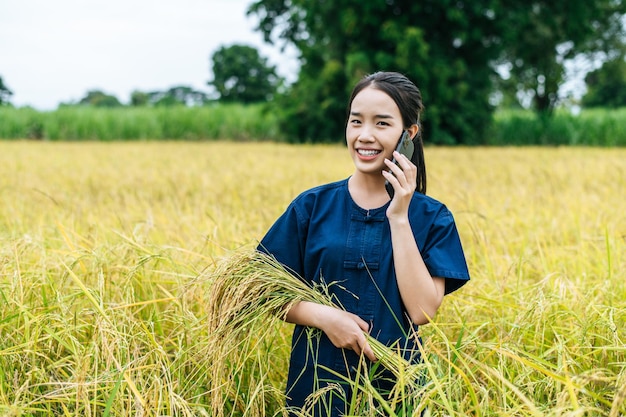 Ritratto di una bella giovane agricoltrice asiatica usa lo smartphone in un campo di riso biologico e sorride con felicità