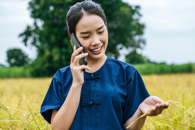 Ritratto di una bella giovane agricoltrice asiatica usa lo smartphone in un campo di riso biologico e sorride con felicità