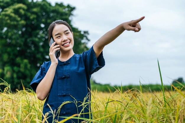 Ritratto di una bella giovane agricoltrice asiatica usa lo smartphone in un campo di riso biologico e sorride con felicità