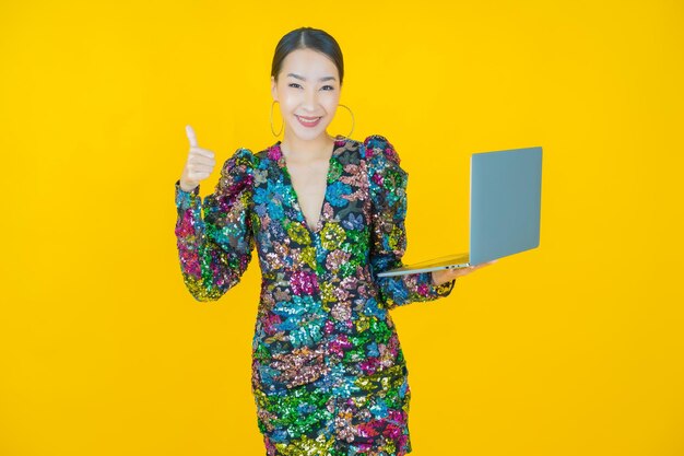 Ritratto di una bella giovane donna asiatica che sorride con il computer portatile acceso su giallo