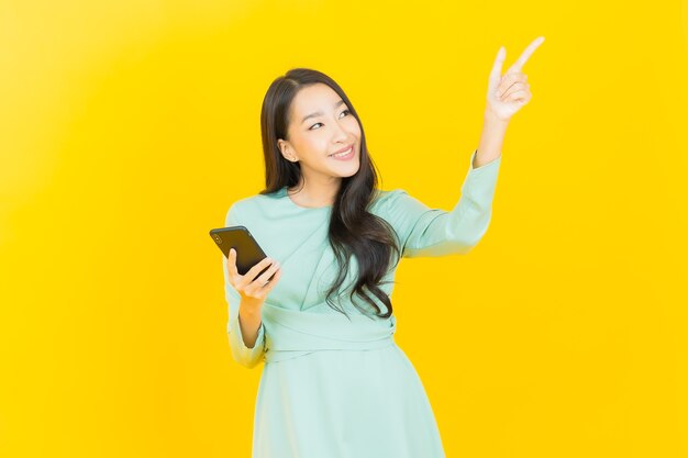 Ritratto di una bella giovane donna asiatica che sorride con un telefono cellulare intelligente su giallo