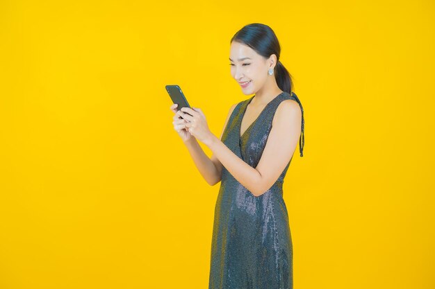 Ritratto di una bella giovane donna asiatica che sorride con un telefono cellulare intelligente su giallo