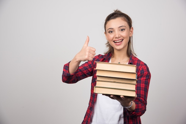 Ritratto di una bella giovane donna che tiene libri e mostra un pollice in su.