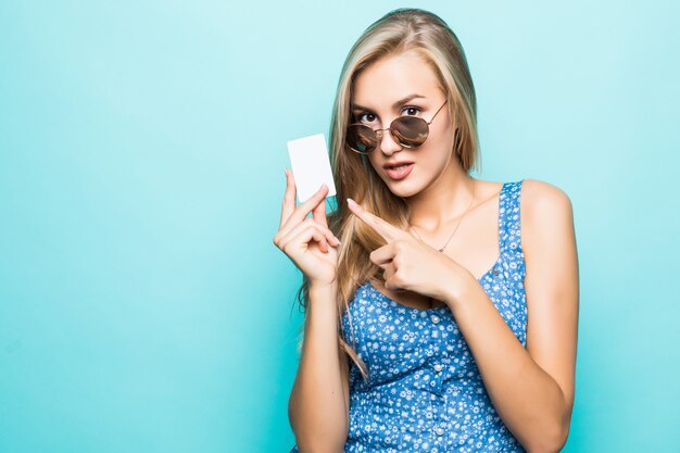 Ritratto di una bella giovane donna vestita di maglione puntare il dito contro la carta di credito isolato su sfondo blu
