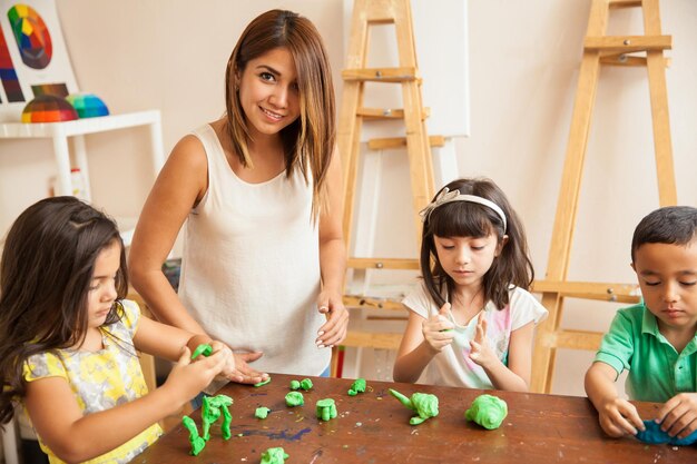 Ritratto di una bella insegnante di latino e dei suoi studenti che lavorano con l'argilla durante la lezione di scultura