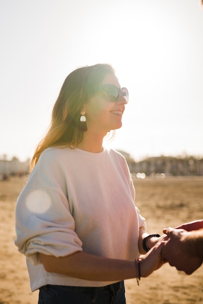 Ritratto di una bella mano sorridente della tenuta della giovane donna del suo ragazzo il giorno soleggiato alla spiaggia