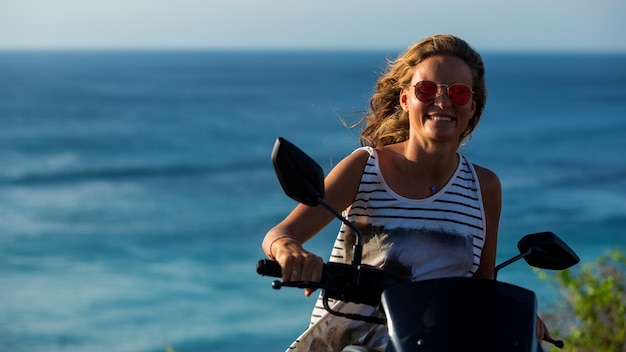 Ritratto di una bella ragazza alla guida di uno scooter su una scogliera con un'incredibile vista sull'oceano.