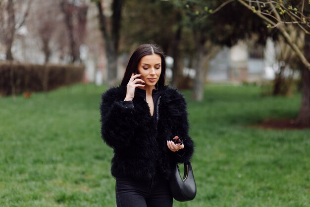 Ritratto di una bella ragazza sorridente con lunghi capelli scuri vestita di nero. Giovane donna utilizzando il telefono cellulare