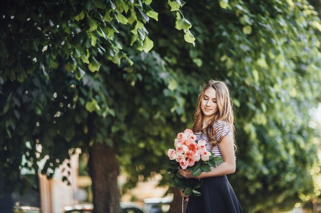 Ritratto di una bellissima giovane donna bionda in piedi con un mazzo di rose