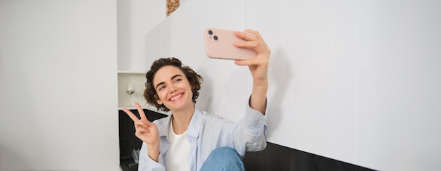 Ritratto di una bellissima ragazza brunetta che si fa un selfie con lo smartphone nella sua cucina posando per una foto