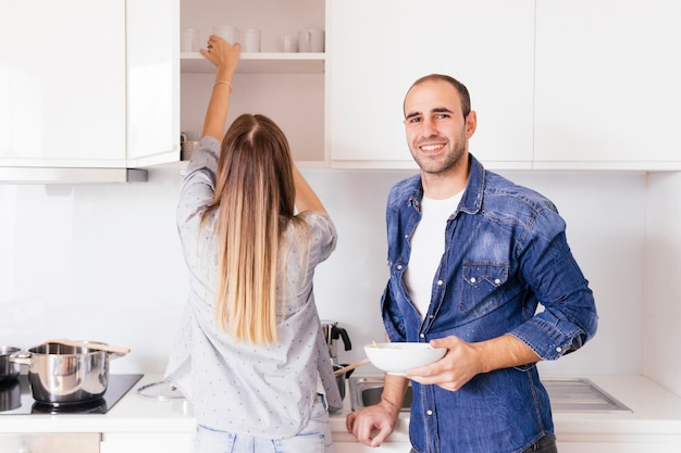 Ritratto di una ciotola sorridente della holding del giovane in mani che si levano in piedi vicino alla sua moglie nella cucina