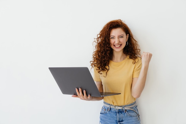 Ritratto di una donna abbastanza giovane che celebra un successo sul computer portatile isolato su priorità bassa bianca