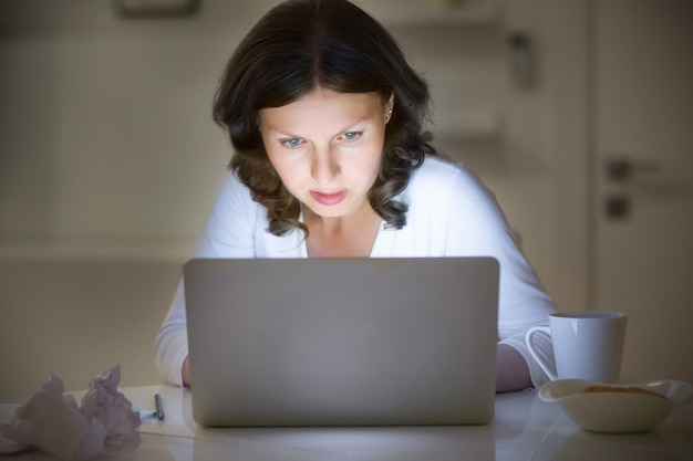 Ritratto di una donna al banco di lavoro con un computer portatile, tarda notte