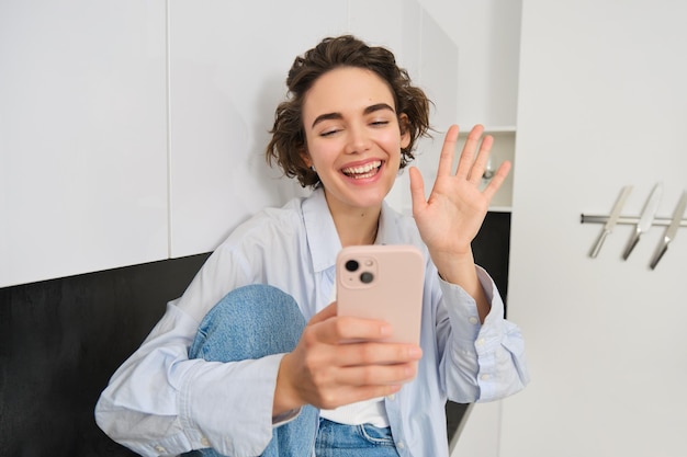 Ritratto di una donna amichevole sorridente che guarda il telefono cellulare e ondeggia il video della fotocamera dello smartphone