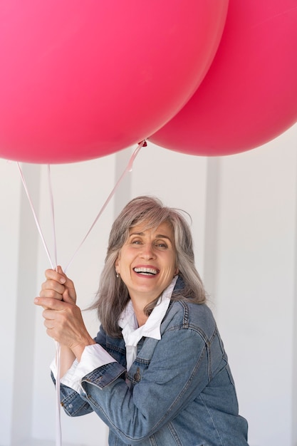 Ritratto di una donna anziana in posa con una giacca di jeans e con in mano palloncini rosa