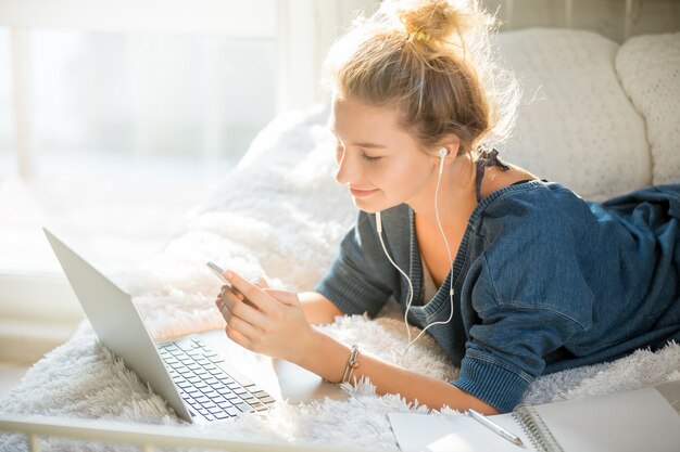 Ritratto di una donna attraente che si trova sul letto con il computer portatile