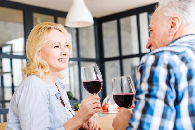 Ritratto di una donna bionda senior che beve il vino con il suo marito nella cucina