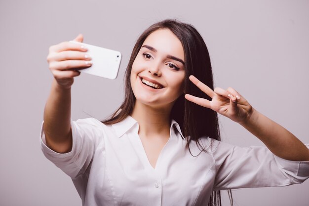 Ritratto di una donna carina sorridente che fa selfie foto sullo smartphone isolato su uno sfondo bianco