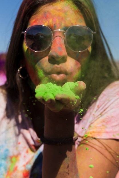 Ritratto di una donna che indossa occhiali da sole che soffia verde polvere di holi