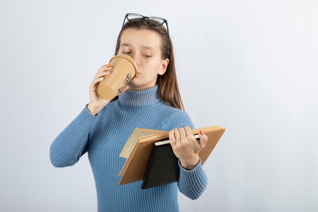 Ritratto di una donna con gli occhiali che legge un libro con una tazza di caffè.