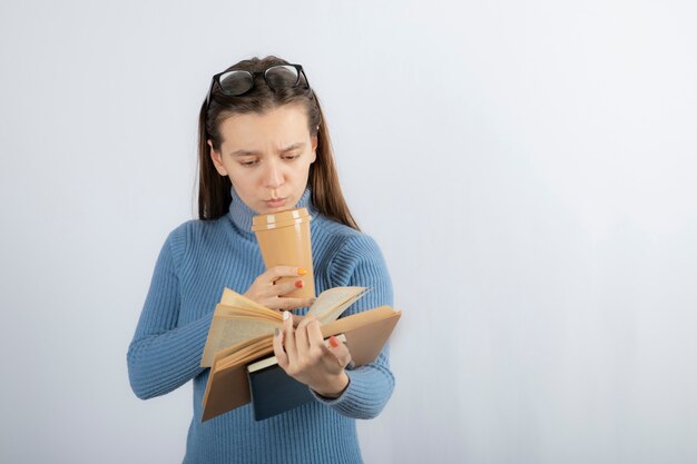 Ritratto di una donna con gli occhiali che legge un libro con una tazza di caffè.