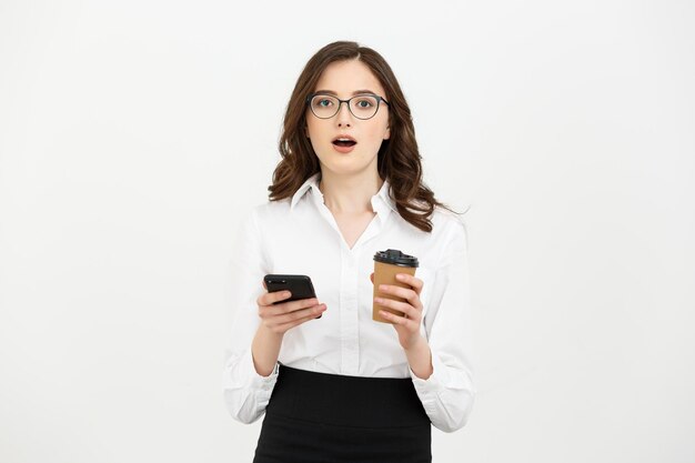 Ritratto di una donna d'affari sorpresa scioccata in occhiali che tengono tazza di caffè da asporto e cellulare