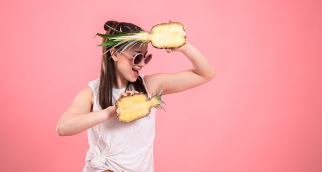 Ritratto di una donna elegante su uno sfondo rosa con ananas nelle sue mani.