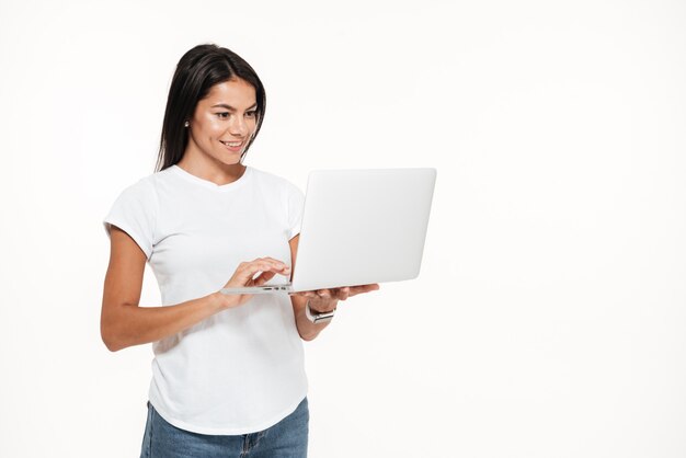 Ritratto di una donna felice che per mezzo del computer portatile mentre stando