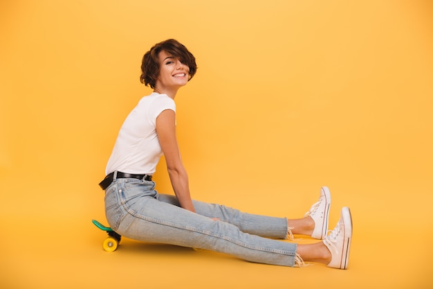 Ritratto di una donna felice eccitata seduta su uno skateboard